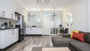 A modern kitchen with white cabinets, a black stove, and a dining area with a gray sofa and a mirror.