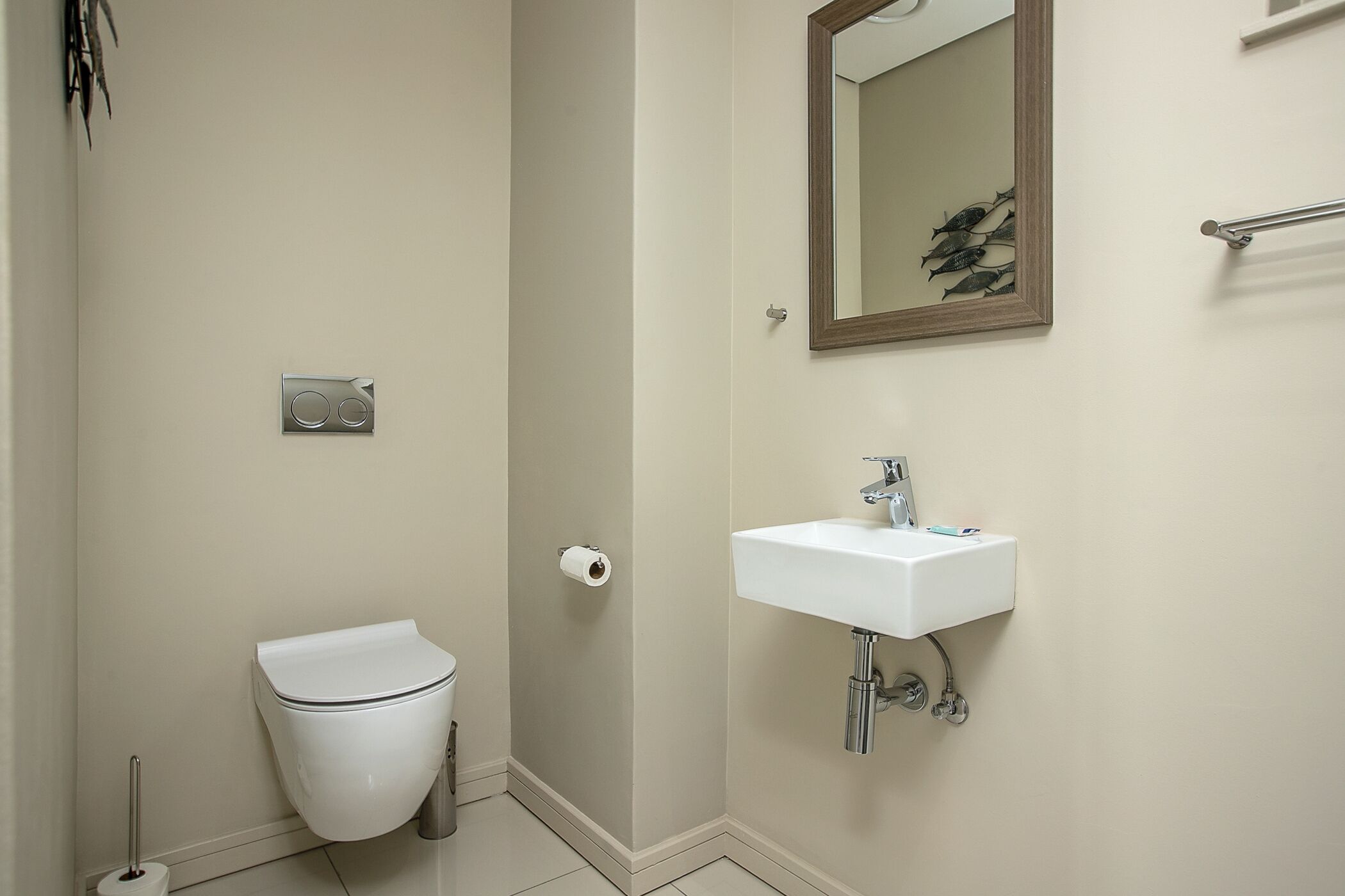 A bathroom with a toilet, a sink, a mirror, and a toilet paper holder.