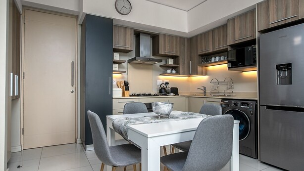 A modern kitchen with a dining table, chairs, a clock, and built-in appliances.