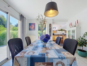 Ein Essbereich mit Tisch, der mit einer Tischdecke im Seestil bedeckt ist, umgeben von Korbstühlen, einer Hängelampe und Blick ins Freie.