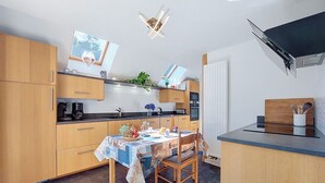 Een compacte keuken met houten kastjes, een eettafel met een tafelkleed met patroon, en een klein kookeiland met een spoelbak.
