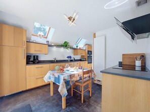 Eine kompakte Küche mit Holdekor-Schränken, einem Esstisch mit gemustertem Tischläufer und einer kleinen Kochinsel mit Spüle.