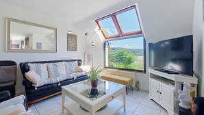 Un salon comprenant un canapé, une table basse, un téléviseur, une grande fenêtre donnant sur un beau paysage et un miroir.