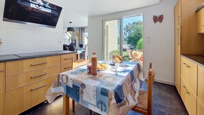 Une cuisine moderne avec une table à manger pour deux, un téléviseur fixé au-dessus du comptoir et une vue sur l’extérieur.