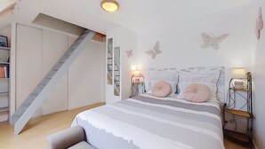 Une chambre à coucher avec un lit, des tables de chevet, une lampe, une bibliothèque et un escalier.
