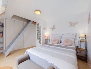 Een slaapkamer met een bed, nachtkastjes, een lamp, een boekenplank en een trap.
