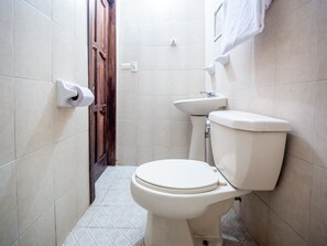 A small, clean bathroom with a toilet, sink, and toilet paper holder. - Posada San Jose (San Pedro Pochutla)
