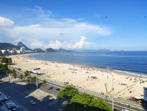 A beach with a road in the foreground and buildings in the background. - TC1001 Vista Perfeita de Copacabana (Rio de Janeiro)
