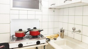 Una cucina con un piano cottura bianco, due pentole rosse, una finestra e un lavandino pieno di utensili.