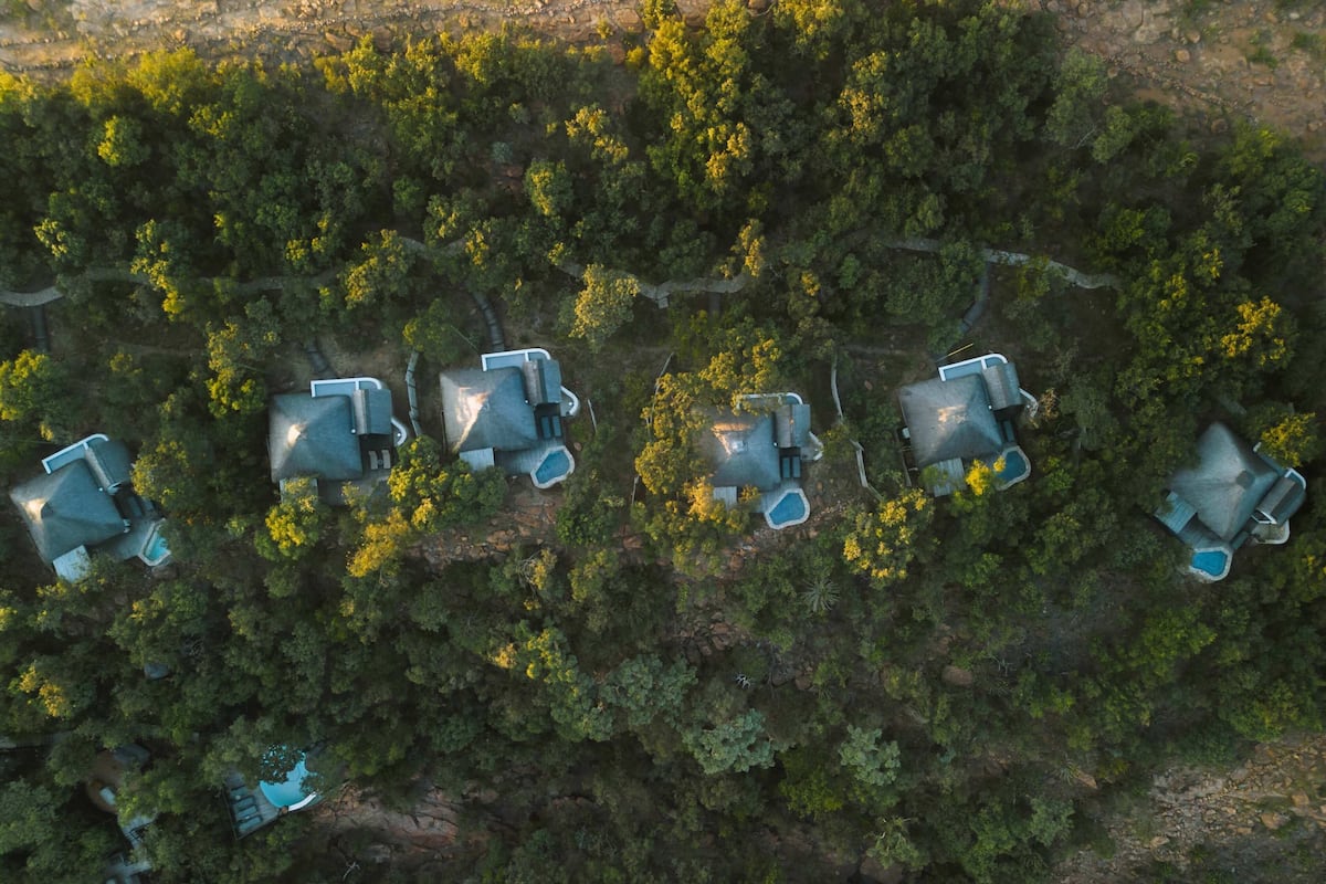 Une vue aérienne d’un ensemble de maisons comprenant plusieurs pièces, entourées d’une forêt dense.