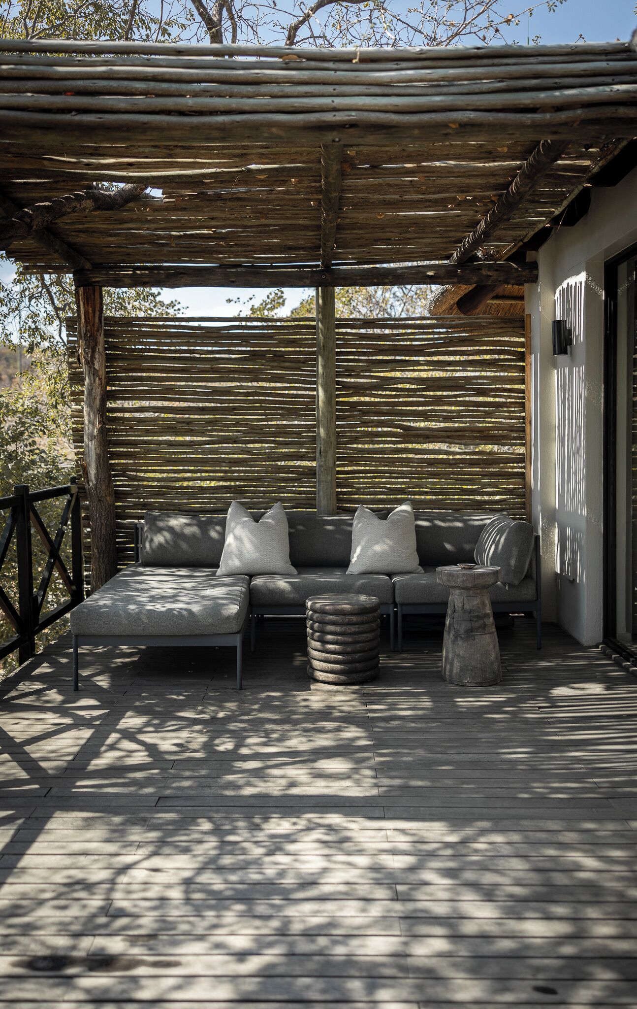 A covered outdoor seating area with a sofa and cushions, a stone table, and a wooden deck.