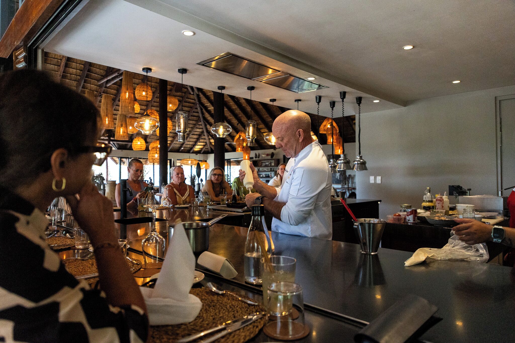 A bar area with a bartender preparing drinks, a counter with various bottles and glasses, and a rustic ceiling with hanging lights.
