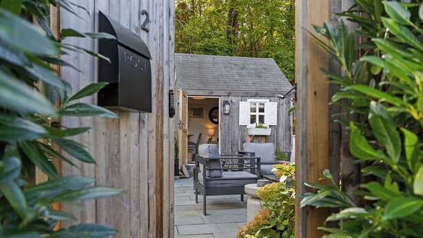 A wooden house with a mailbox, a small porch with a chair, and a garden area.