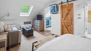 A modern bedroom with a loft-style ceiling, a large window, a sliding barn door, a walk-in closet, and a view of the city.