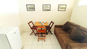 Un espacio habitable compacto con una mesa de comedor, dos sillas, un sofá marrón y un refrigerador blanco. Hay tres cuadros en la pared.