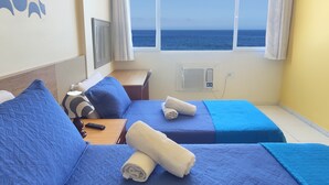 Una habitación con dos camas, televisión, ventana con vista al mar y aire acondicionado.