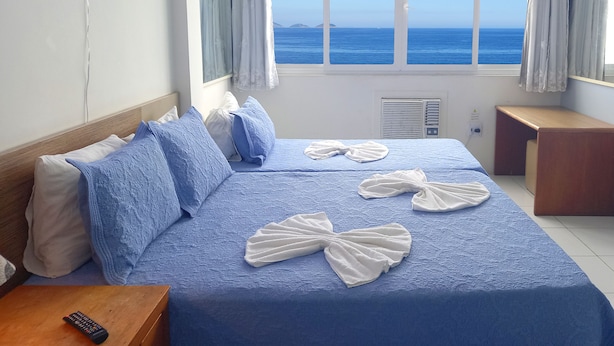 A hotel room with a large bed, a bedside table, a nightstand, a window with a view of the sea, and a neon sign on the wall. - TC1203 Janela para o Mar (Rio de Janeiro)