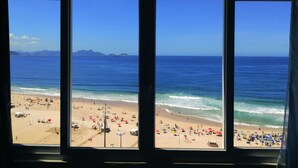 A beach view through a window with a clear sky, calm sea, and beachgoers. - TC1203 Janela para o Mar (Rio de Janeiro)