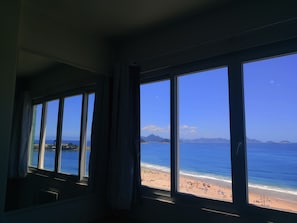Een kamer met grote ramen met uitzicht op een strand.