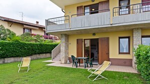 Ein zweistöckiges Gebäude mit einem Balkon, einer kleinen Sitzgelegenheit im Freien inklusive Stühle und einer Treppe, die zum Eingang führt.
