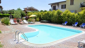 Ein Swimmingpool mit einer Pflasterterrasse, Liegestühlen und einem kleinen Tisch mit Sonnenschirm.