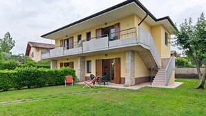 Ein zweistöckiges Haus mit Balkon, Treppe und einer kleinen Außen-Sitzgelegenheit.