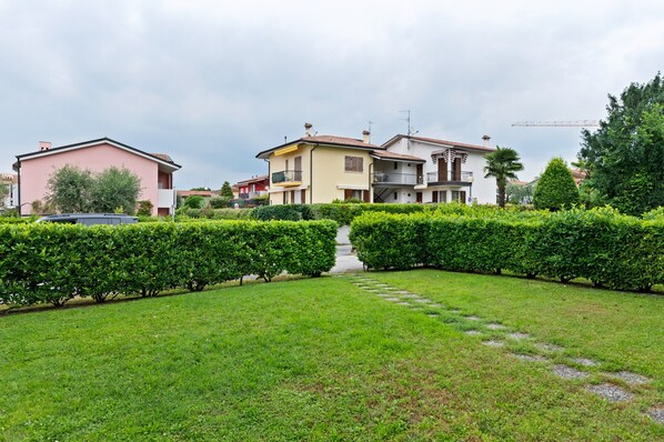 A residential area with a well-maintained lawn, hedges, and a pathway leading to a row of houses.