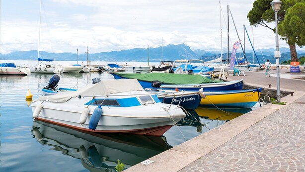 Ein Yachthafen mit vertäuten Booten, ruhigem Wasser und Bergen im Hintergrund.