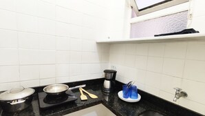 Een keuken met witte betegelde wanden, een zwart aanrecht, een fornuis, een koffiezetapparaat en een spoelbak.