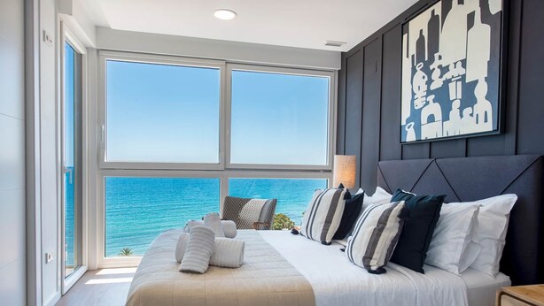 A bedroom with a large bed, a view of the ocean, and a cityscape painting on the wall. - Modern stunning views sea front SEA WATER APARTMENT (Alicante)
