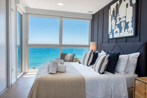 A bedroom with a large bed, a view of the ocean, and a cityscape painting on the wall. - Modern stunning views sea front SEA WATER APARTMENT (Alicante)
