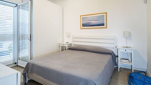 Ein Schlafzimmer mit einem Bett, Nachttischen, einer Lampe, einem Bild und einer blauen Tasche.