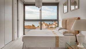 Un dormitorio con un ventanal grande, una cama, una mesita de noche y una lámpara.