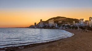 Una playa con un paisaje urbano al fondo, incluyendo edificios y una colina.