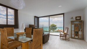 Una sala de estar moderna con una mesa de comedor de vidrio, sillas de mimbre, un sofá y vista al mar a través de amplios ventanales.