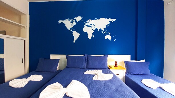 Habitación de hotel con dos camas, un mapa del mundo en la pared y una mesita de noche con lámpara.