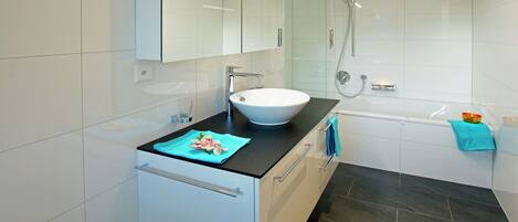 Ein modernes Badezimmer mit einem weißen Waschbecken, einer dunklen Arbeitsplatte und einer Duschkabine.