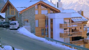 Un edificio cubierto de nieve con fachada de piedra y balcones de madera, rodeado de montañas.