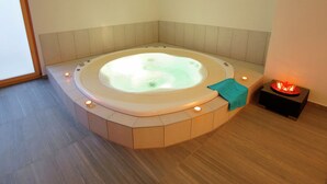 Un baño moderno con una bañera hidrotermal central, una mesita con velas y vistas al exterior a través de un ventanal amplio.