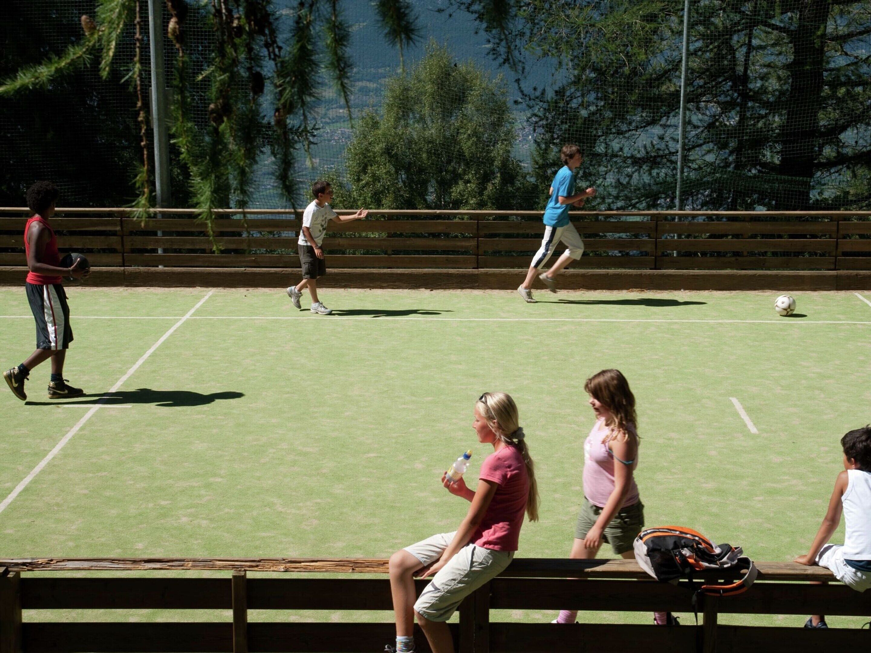 A sports field with a netted fence, a bench, and a water bottle on the ground.