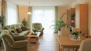 Ein Wohnzimmer mit einer Couch, einem Sessel, einem Couchtisch und einem Esstisch mit einem Blumenstrauß.