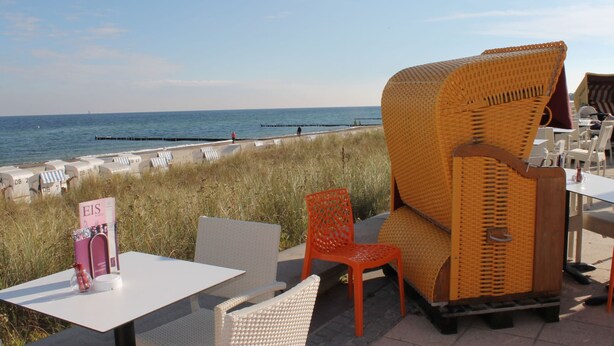 An outdoor seating area with wicker chairs and tables, overlooking a beach with a clear sky. - Modernes Apartment in Kuehlungsborn mit Garten (Kuehlungsborn)