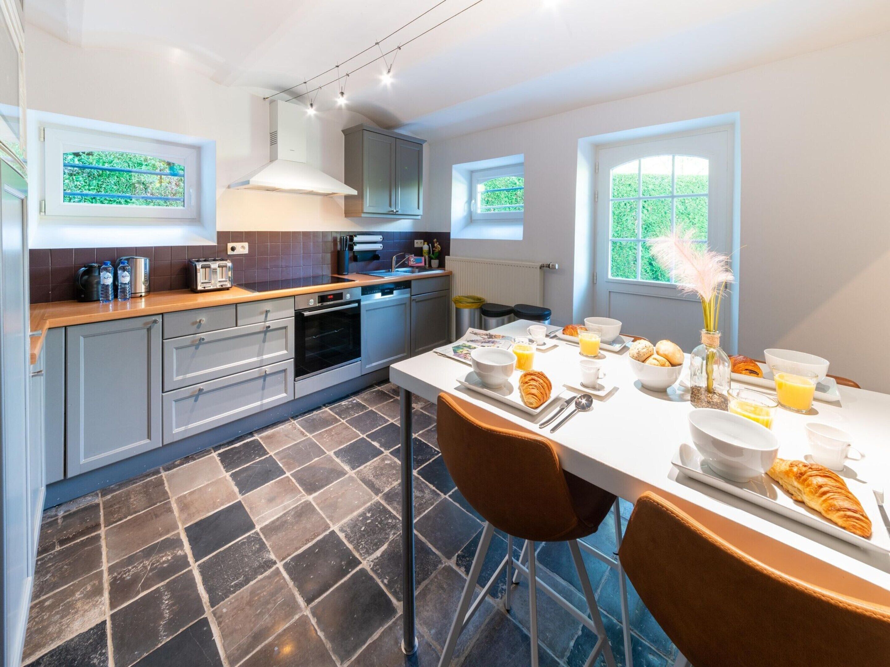 A modern kitchen with grey cabinets, a built-in oven, and a dining area with a table set for breakfast.