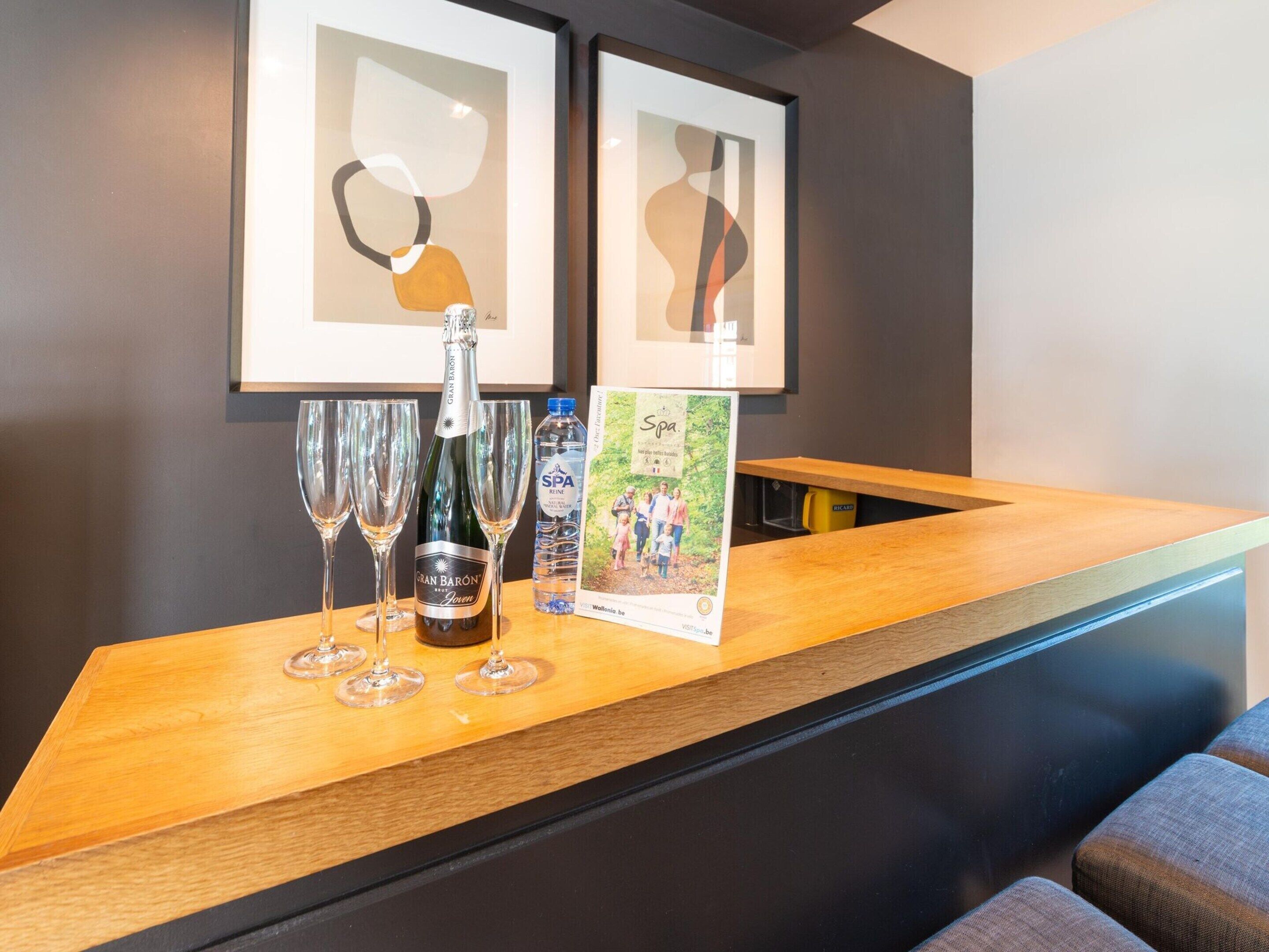 A reception area with a wooden counter, a bottle of Gran Baron wine, four wine glasses, a water bottle, and a printed brochure.