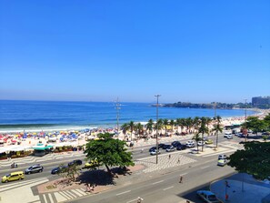 Une vue sur la plage, avec une route, des parasols, des palmiers et un ciel bleu dégagé.