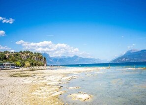 A beach with clear water, a rocky shoreline, and mountains in the background.