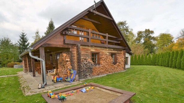 A log cabin with a wooden deck, a play area with toys, and a neatly trimmed lawn.