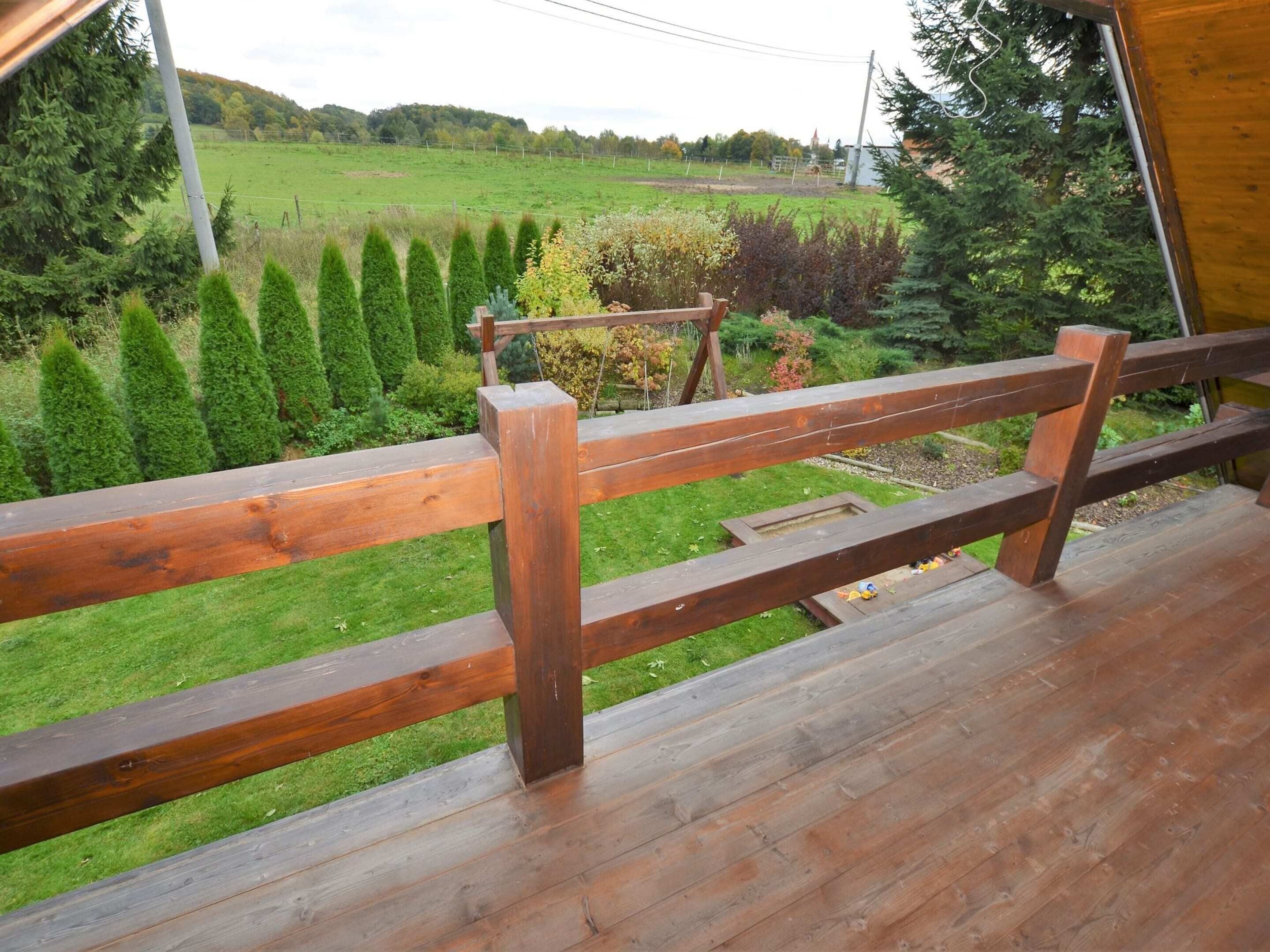 A wooden deck with a view of a green field and trees.