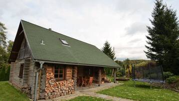 A log cabin with a green roof, stone foundation, and a porch with outdoor furniture.