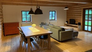 A cozy log cabin interior with a wooden dining table, a sofa, and a television.